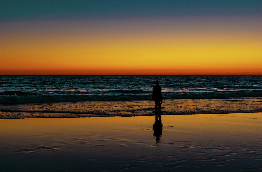 Young woman watches a wonderful sunset as the sea wets her feet in ...