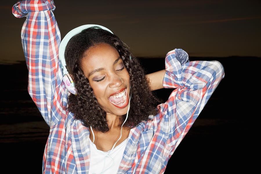 Young woman wearing headphones arm raised, eyes closed open mouthed smiling Photograph by Duel