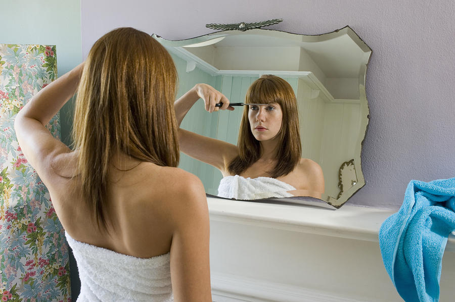Young woman wearing towel cutting fringe in mirror, rear view Photograph by Tara Moore