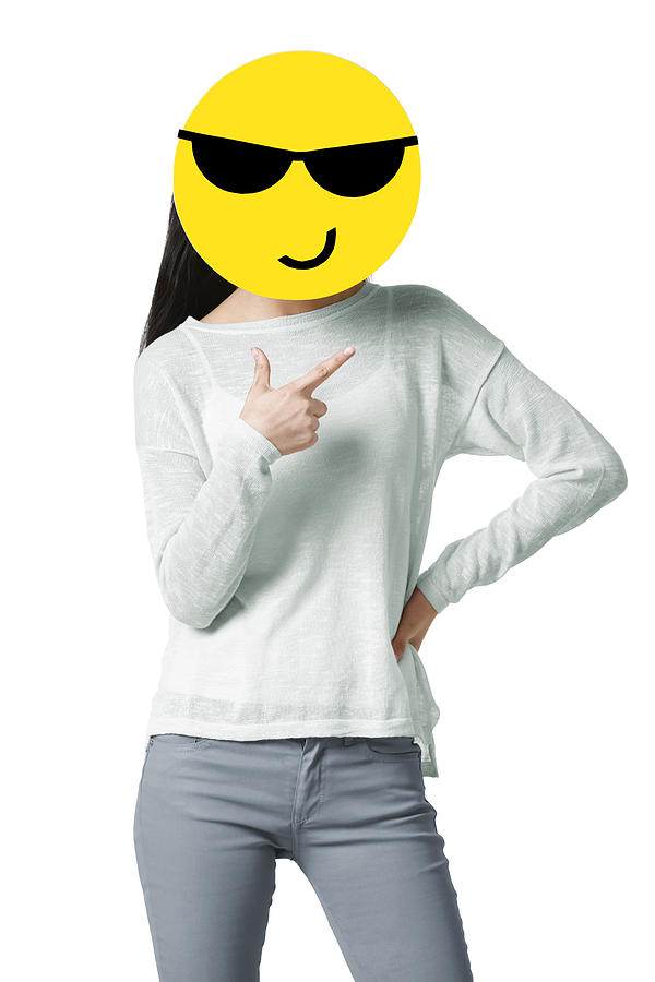 Young woman with a cool emoticon face in front of her face Photograph by BJI / Blue Jean Images