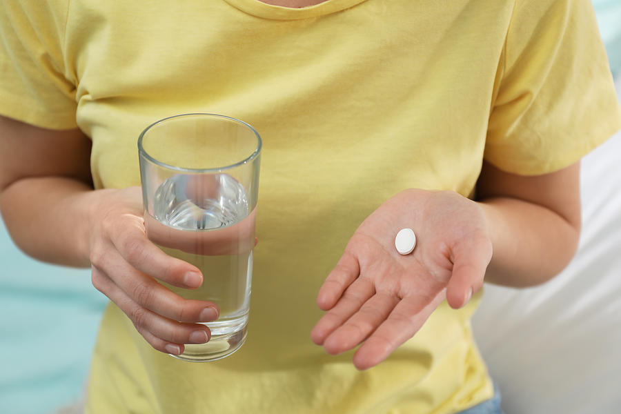 Young woman with abortion pill and glass of water on blurred background, closeup Photograph by Liudmila Chernetska
