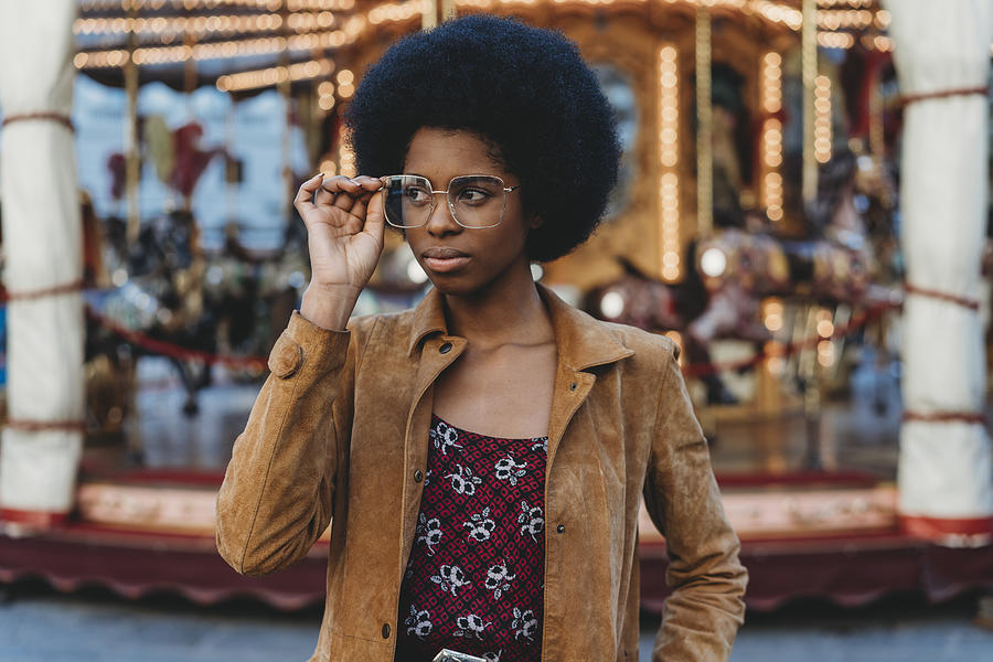 Young woman with afro hair putting on spectacles in front of carousel Photograph by Lorenzo Antonucci