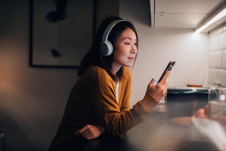 Young Woman With Bluetooth Headphones Listening To Music On Smartphone Photograph by Oscar Wong