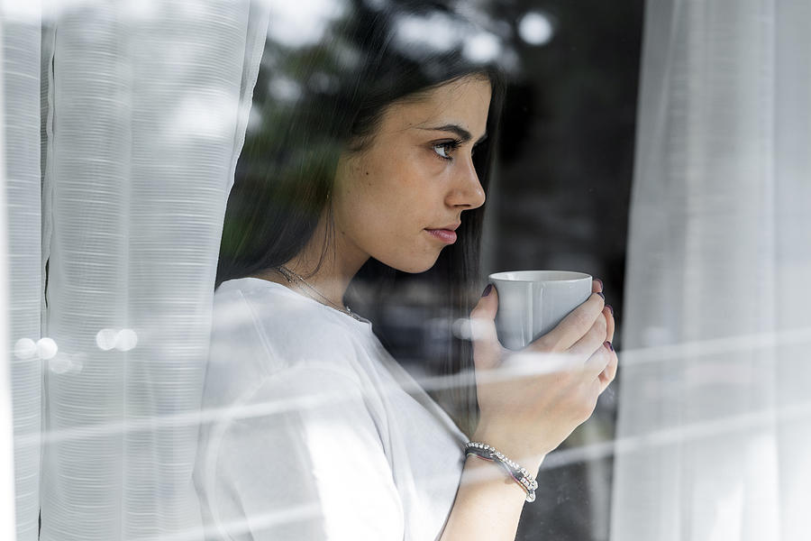 Young woman with cup of coffee behind windowpane Photograph by Westend61