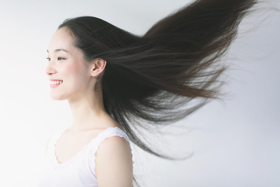 Young woman with fluttering hair smiling Photograph by Yosuke Tanaka/Aflo