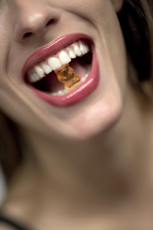 Young woman with gummi bear in mouth, portrait Photograph by Patrick Jelen