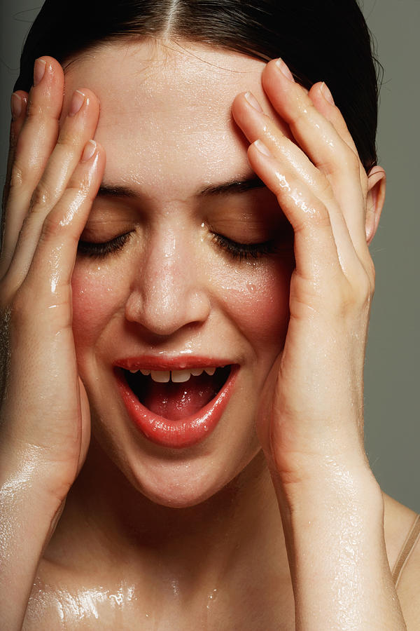 Young woman with hands on face perspiring, close-up Photograph by Marili Forastieri