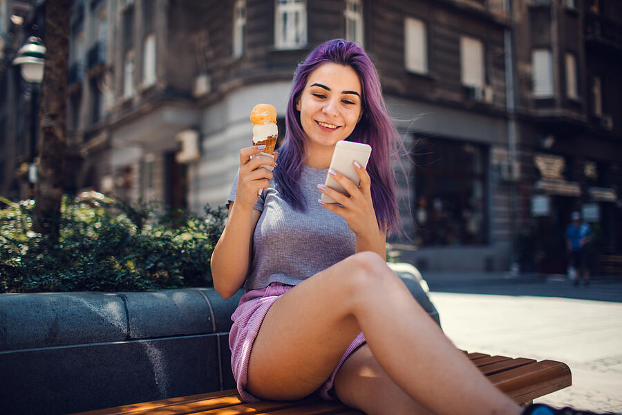 Young Woman With Purple Hair Eating Ice Cream And Using Smart Phone Photograph by Vgajic