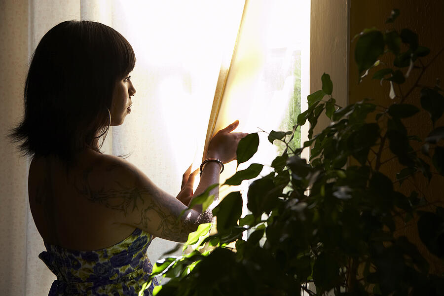 Young woman with tattoo looking out window Photograph by Thomas Northcut