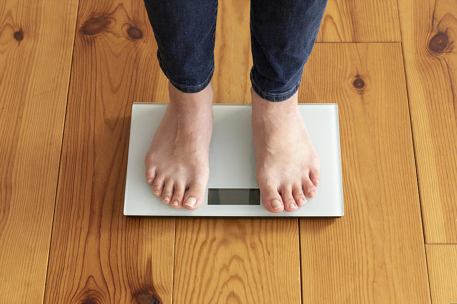 Young womans feet on wooden floor and weight scale Photograph by West