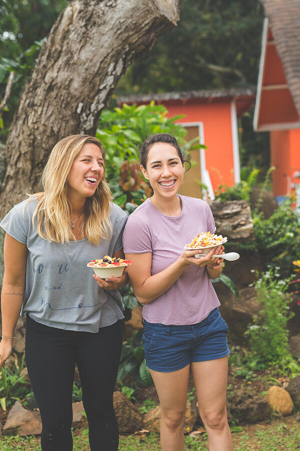 Young women holding smoothie bowls with fresh tropical fruit outdoors Photograph by FatCamera