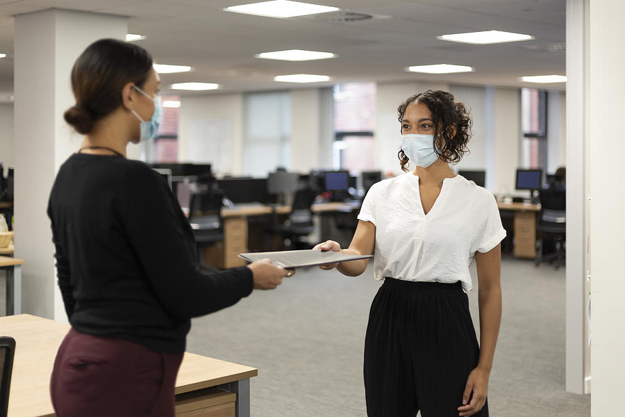 Young women working in an office wearing facemasks Photograph by Kelvinjay